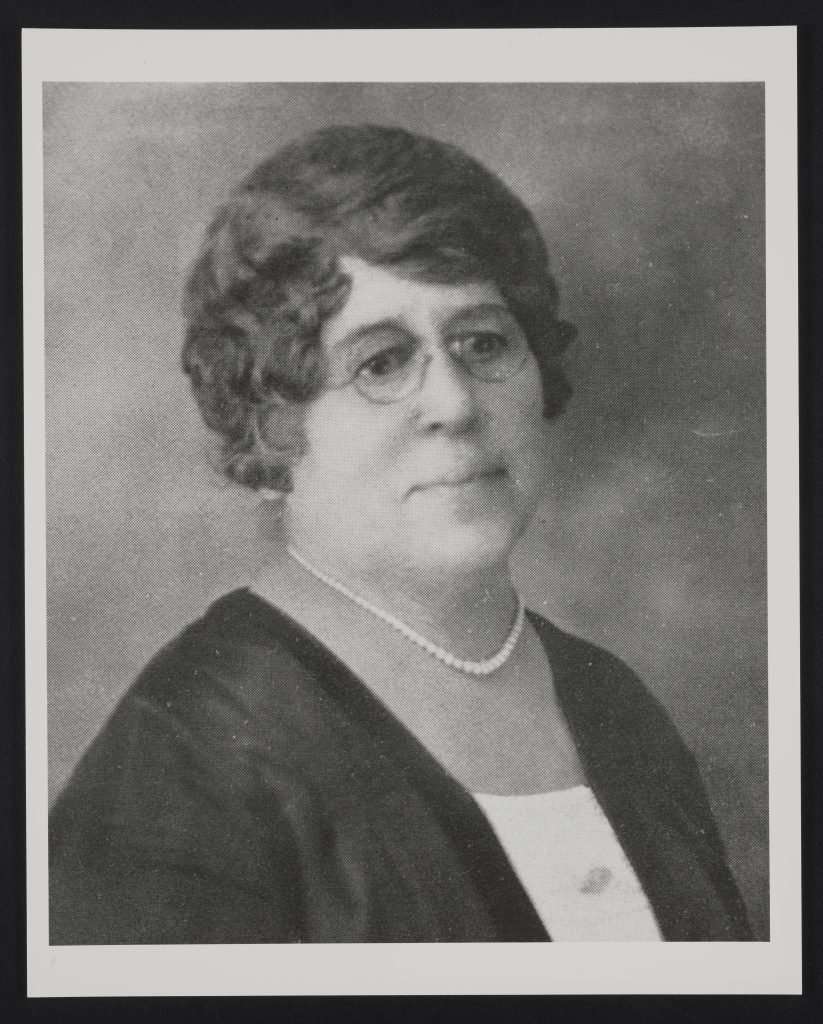 Formal photographic portrait of Jamie Porter Aurora Barrett wearing glasses and a pearl necklace