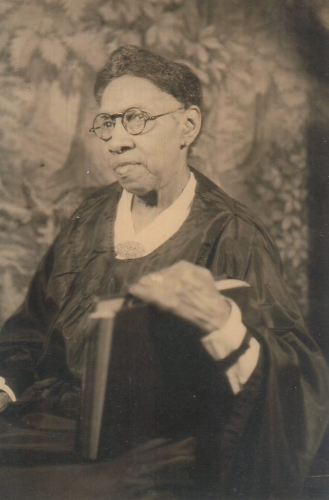 Formal three-quarter photographic portrait of Rosa Armstead holding up a large book in one hand