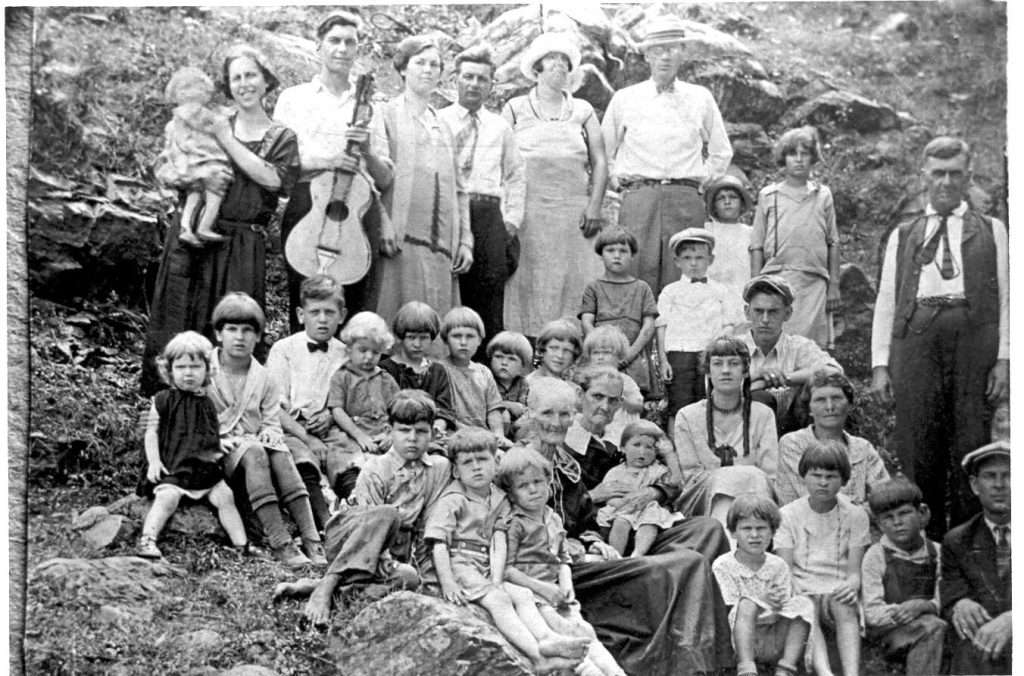 B&W photo of large family with adults standing at back and dozens of children sitting on the ground