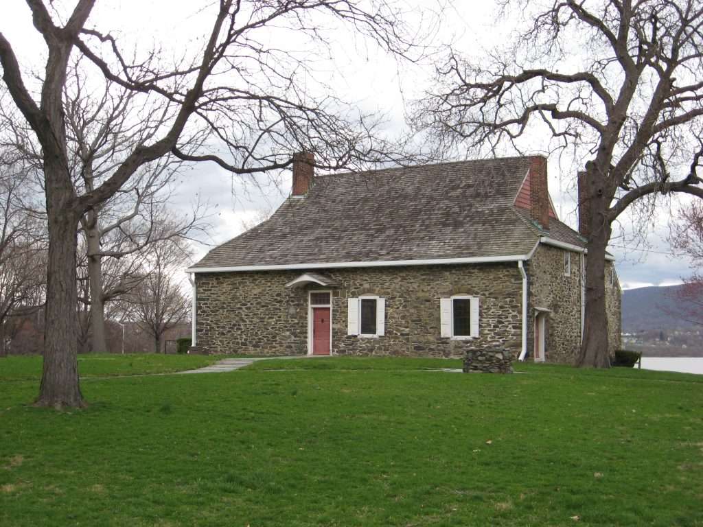 Exterior of Washington's Headquarters Historic Site in New York, a gray stone house on a green lawn overlooking the Hudson River.